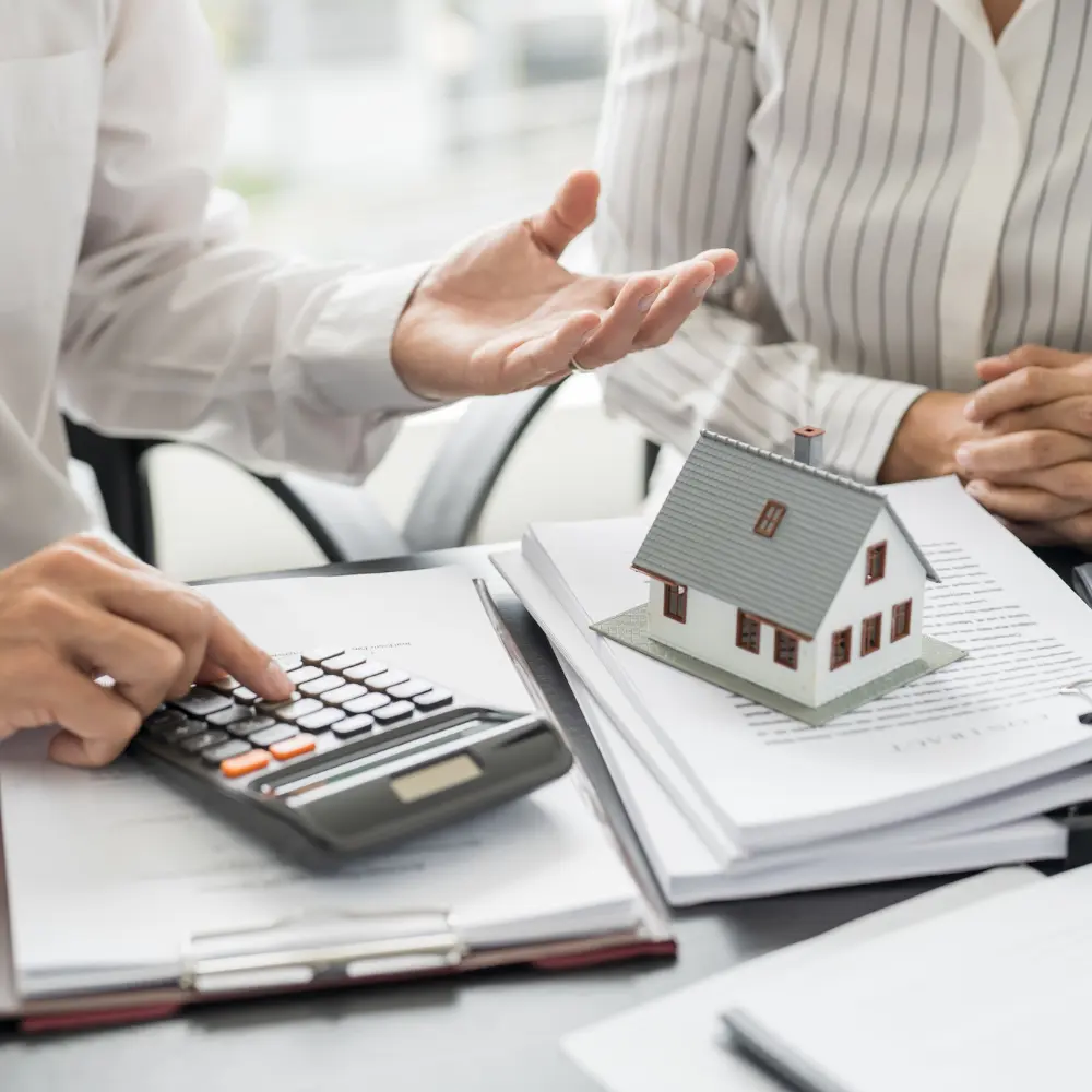 Real estate financial review with calculator, documents, and a model house on a desk.
