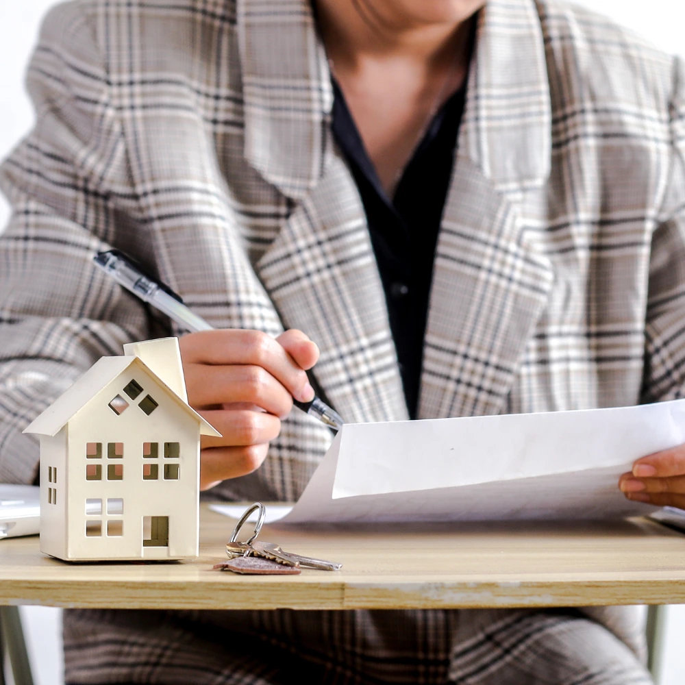 Advisor reviewing real estate documents with a small model house and keys on the table.